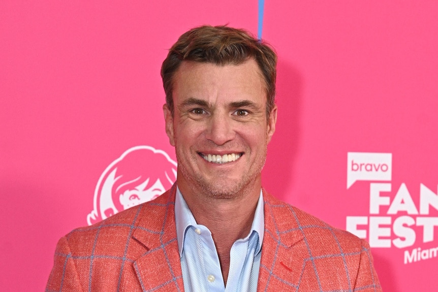 Shep Rose smiling in front of a step and repeat at Bravo Fan Fest 2024.