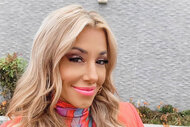 Danielle outdoors, smiling, in a multi-colored turtleneck and coral colored blazer.