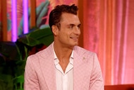 James Kennedy smiling in a pink suit in front of plants and curtains.