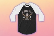 A baseball tee with the copy "RHONJ Go Team" in front of a fading pink background.