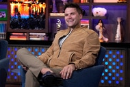 Tom Schwartz sits in a chair and wears a brown jacket on the set of WWHL