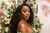 Jassi Rideaux posing in an emerald green gown in front of a backdrop of flowers.