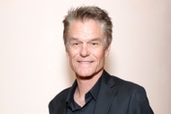 Harry Hamlin wearing a black suit in front of a beige backdrop