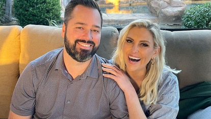 Gina Kirschenheiter and Travis Mullen sitting on a couch together laughing.