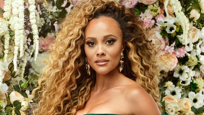 Ashley Darby posing in an emerald green gown in front of a backdrop of flowers.