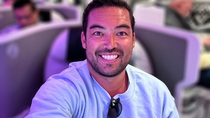 Colin Macrae wearing a blue shirt, smiling while sitting in first class on a flight