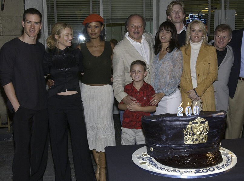 Young Garcelle with a group of actors standing together and posing amongst a large cake.