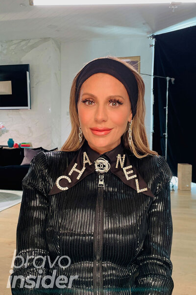 Dorit Kemsley sitting and posing in a black, Chanel, outfit.