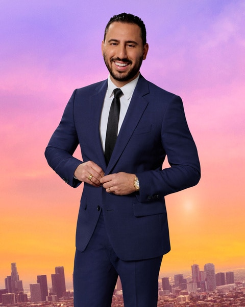 Josh Altman wearing a blue blazer in front of a purple and pink sky and the LA city scape.