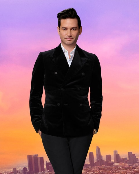 Josh Flagg wearing a black blazer in front of a purple and pink sky and the LA city scape