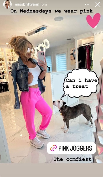 Brittany Mattessich wearing hot pink sweatpants and white tank top with her dog while standing in her closet.