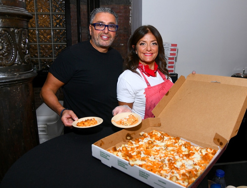 Kathy Wakile and Rich Wakile posing next to a large pizza.