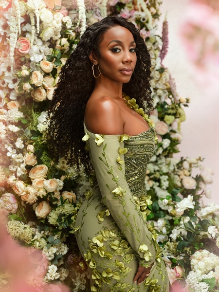 Jassi Rideaux posing in a green gown in front of a backdrop of flowers.