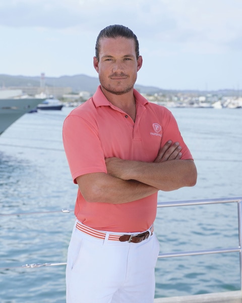 Gary King posing in uniform onboard the Parsifal 3 in front of a marina.