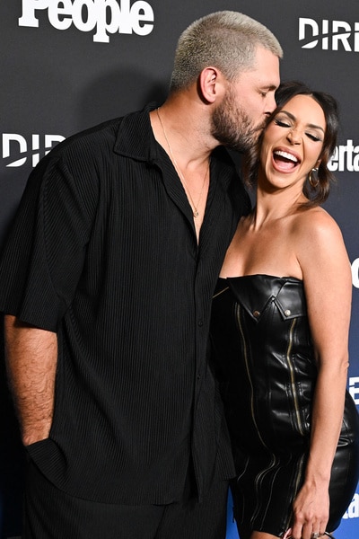 Scheana Shay and Brock Davies embracing each other in front of a step and repeat at an event.