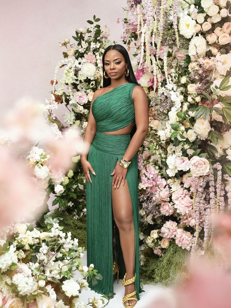 Keiarna Stewart posing in an emerald green gown in front of a backdrop of flowers.