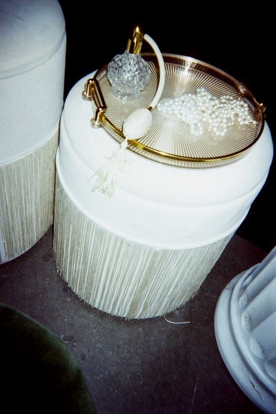 A glass perfume bottle and pearl necklace on a gold tray sitting atop a vintage stool