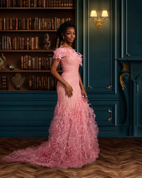 Full length of Venita Aspen wearing a pink gown standing in front of a book shelf