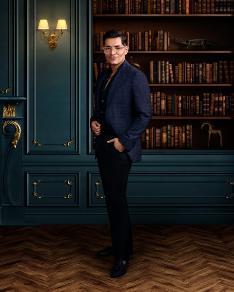 Full length of Rodrigo Reyes wearing a suit standing in front of a book shelf