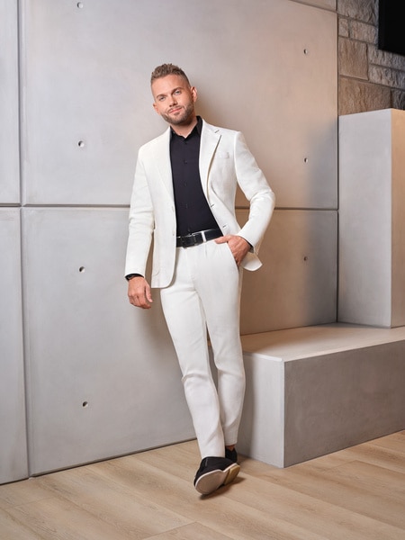 full length of Kenny Sperry wearing a white suit in front of a grey wall