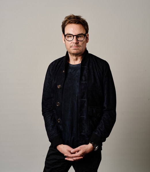 Whitney Sudler Smith wearing a denim jacket and a black tee shirt in front of a beige backdrop