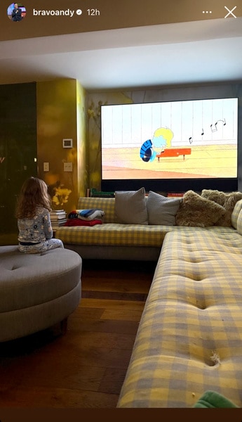 A large screen and Lucy Cohen sitting in Andy Cohen's living room