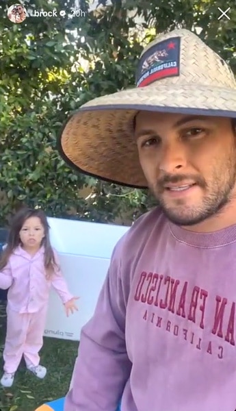 Brock Davies wearing a straw hat with his daughter Summer Moon standing behind him in their backyard