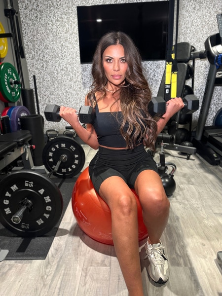 Dolores Catania wearing a black sports bra and black shorts lifting weights in a gym