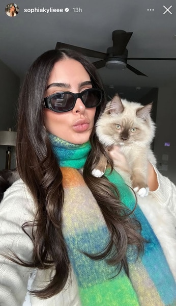 Sophia Umansky wearing sunglasses and a scarf, cuddled up next to her cat.