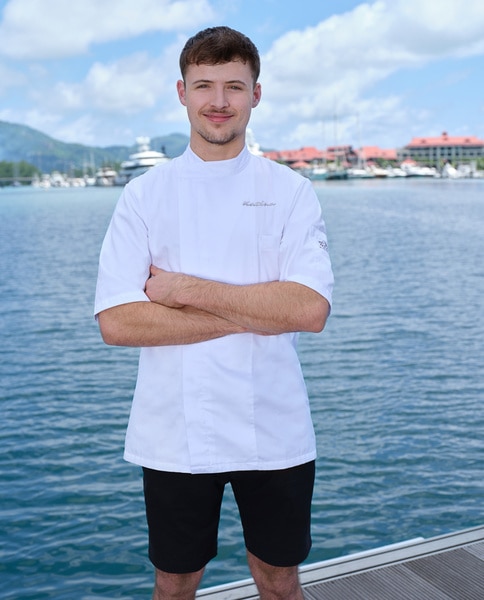 Anthony Bird wearing his chef's uniform in front of water and a marina