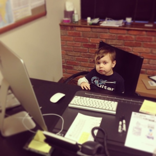 A baby Nicholas Laurita sitting behind a desk in front of a computer monitor and keyboard