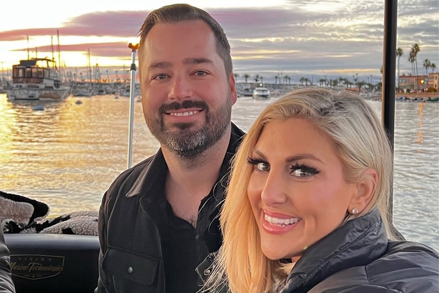 Gina Kirschenheiter and Travis Mullen smiling together on a boat during sunset.