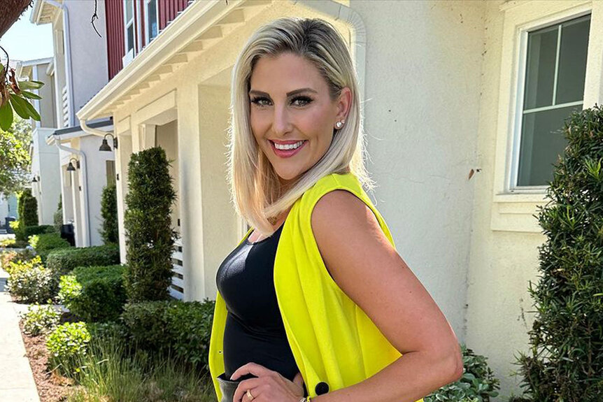 Gina Kirschenheiter smiling and posing in a black outfit with neon yellow in front of a building.