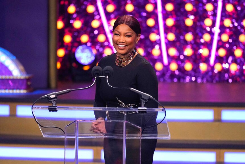 Garcelle Beauvais smiling at the podium on stage during The Bravos at BravoCon 2023.