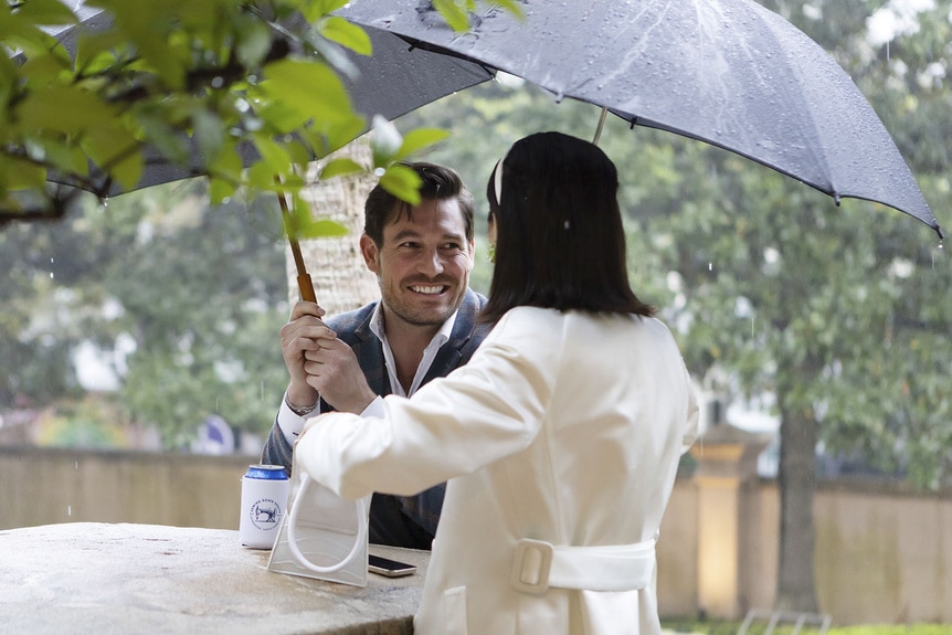 Craig Conover and Paige DeSorbo talk together while holding umbrellas.