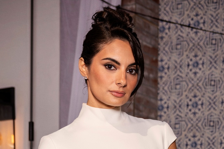 Paige DeSorbo posing in a white gown in front of a themed set.