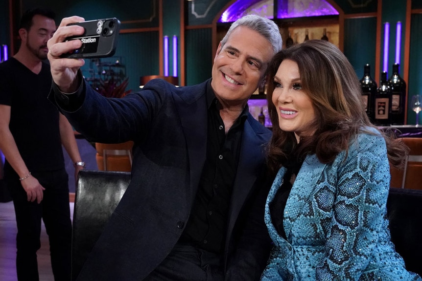 Andy Cohen holds up his cellphone while standing next to Lisa Vanderpump at the VPR reunion