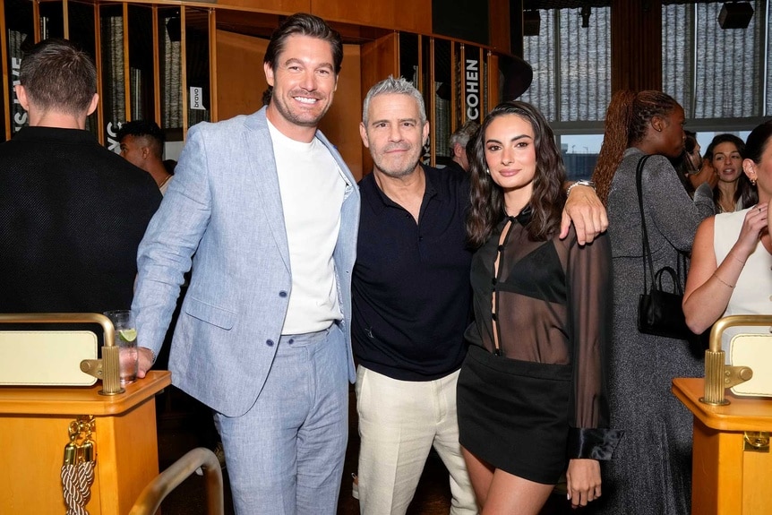 Craig Conover and Andy Cohen with his arm around Paige DeSorbo with party guests behind them