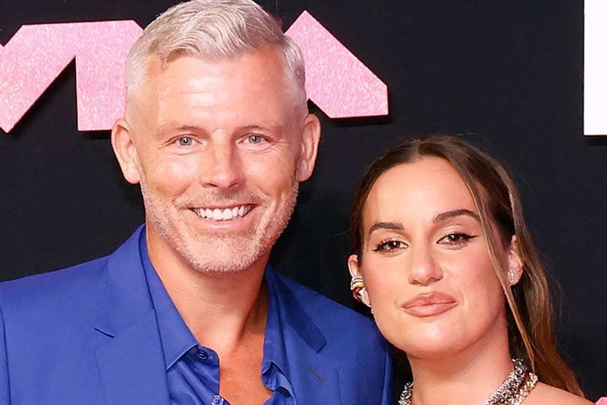 Hannah Berner and Des Bishop smiling next to each other in front of a step and repeat.