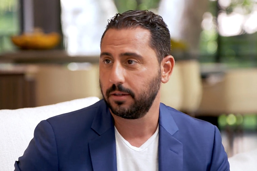 Josh Altman wearing a navy blazer while having a conversation with a client.