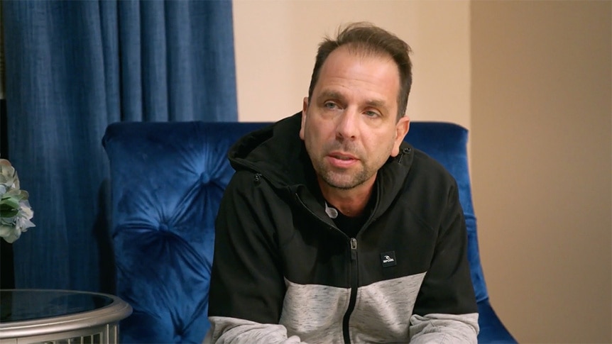 Shane Simpson sitting in his living room on a chair.