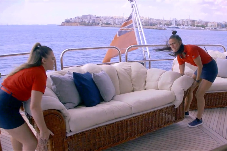 Aesha Scott and Bri Muller moving a couch on a yacht charter.