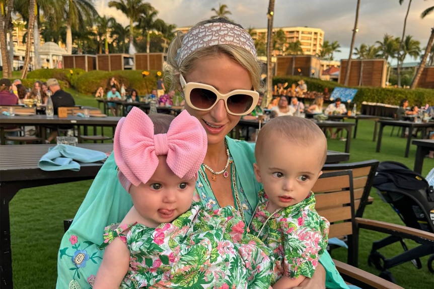 Paris Hilton sitting outdoors holding her kids on her lap.