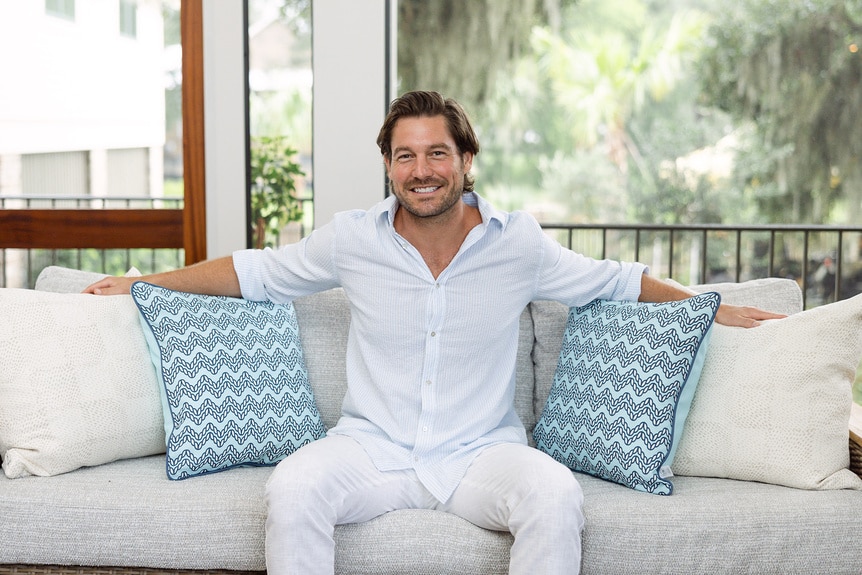 Craig Conover of Southern Charm smiles on a white couch.