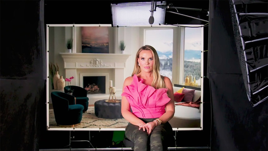 Heather Gay sitting on set in front of a living room background.