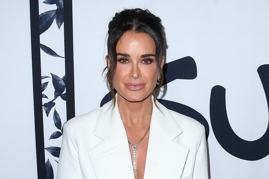 Kyle Richards stares straight in a white blazer at a fashion show