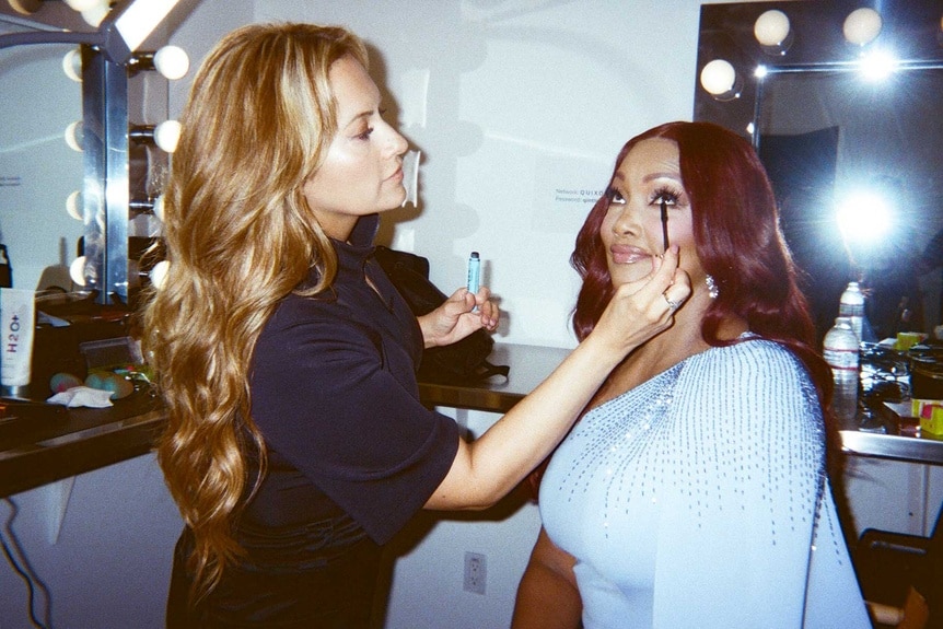 A makeup artist applies mascara to Garcelle Beauvais backstage at the RHOBH Season 14 press shoot