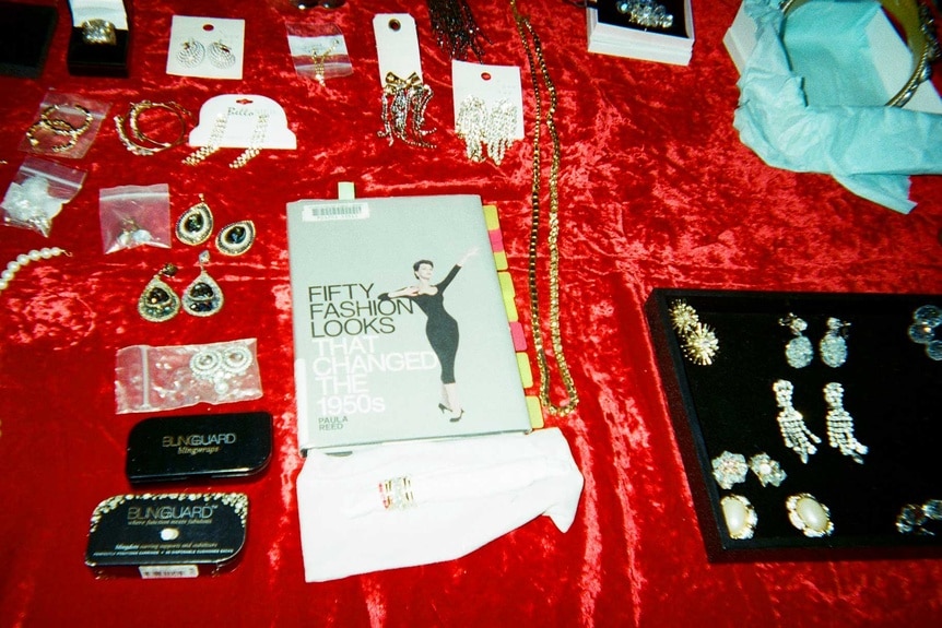 A book surrounded by accessories and jewelry on a table backstage at The Real Houseewives of Beverly Hills Season 14 press shoot