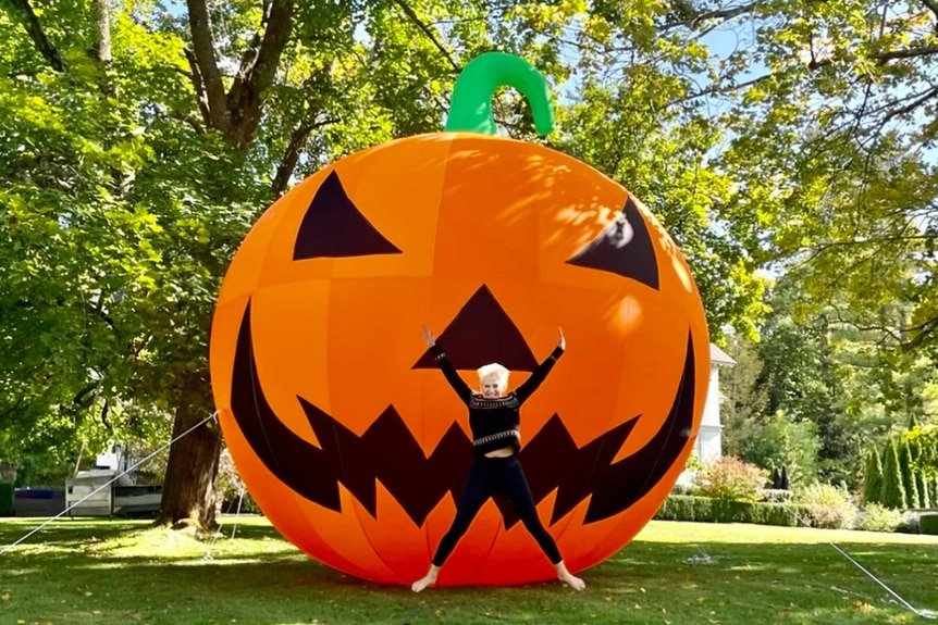 Dorinda Medley jumping in the air in front of a giant inflatable Halloween Jack-O-Lantern