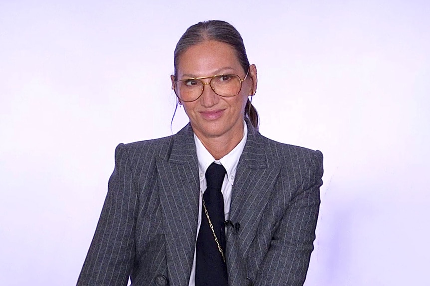 Jenna Lyons wearing a grey pinstripe suit in front of a purple backdrop.